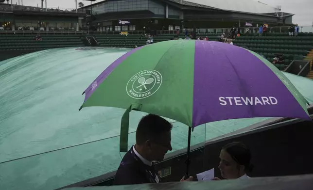 Stewarts cover under an umbrella at a covered court as the start of play is delayed due to rain during the Wimbledon Tennis Championships in London, Wednesday, July 2, 2025.(AP Photo/Kin Cheung)