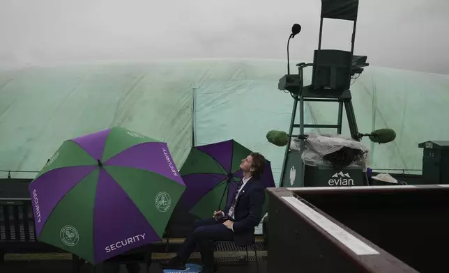 Stewarts sit under an umbrella near a covered court as the start of play is delayed due to rain during the Wimbledon Tennis Championships in London, Wednesday, July 2, 2025.(AP Photo/Kin Cheung)