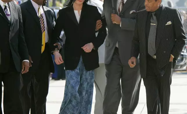 FILE - Michael Jackson, center, is supported by his security personnel as he walks into the courthouse with his father Joe Jackson, right, after arriving late at Santa Barbara County Superior Court, in this March 10, 2005, in Santa Maria, Calif. Jackson was acquitted in 2005 of molesting a 13-year-old cancer survivor at his Neverland Ranch. (AP Photo/Kimberly White, Pool, File)
