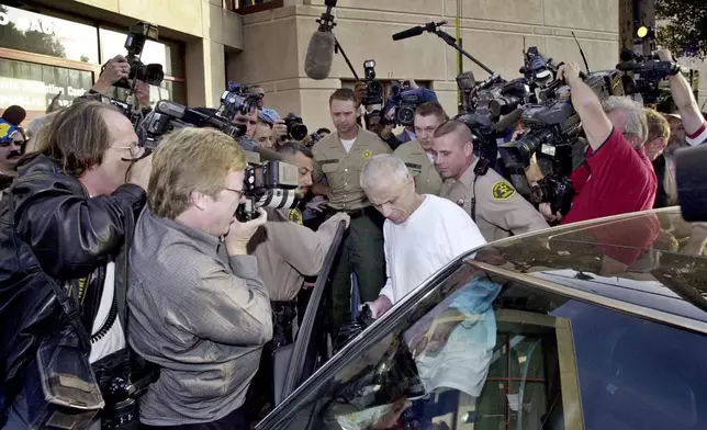 FILE - Escorted by sheriff's deputies, Robert Blake is surrounded by a crowd of photographers and reporters as he gets into his attorney's car after his release from jail to await his murder trial, in downtown Los Angeles, March 14, 2003. (AP Photo/Nick Ut, File)