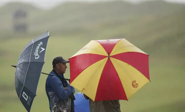 Spectators take cover under an umbrellas as play is suspended due to a thunderstorm waring during a practice round for the 2025 British Open golf championship at the Royal Portrush Golf Club, Northern Ireland, Monday, July 14, 2025. (AP Photo/Francisco Seco)