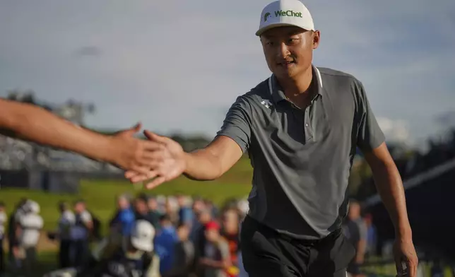 Li Haotong of China taps hands with members of the public as he walks to the 18th tee during the third round of the British Open golf championship at the Royal Portrush Golf Club, Northern Ireland, Saturday, July 19, 2025. (AP Photo/Francisco Seco)