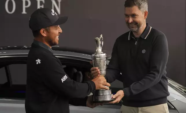 Xander Schauffele of the United States, left, winner of the 2024 British Open, hands back the Claret Jug trophy to the R&amp;A CEO Mark Darbon ahead of the 2025 British Open golf championship at the Royal Portrush Golf Club, Northern Ireland, Monday, July 14, 2025. (AP Photo/Fransisco Seco)