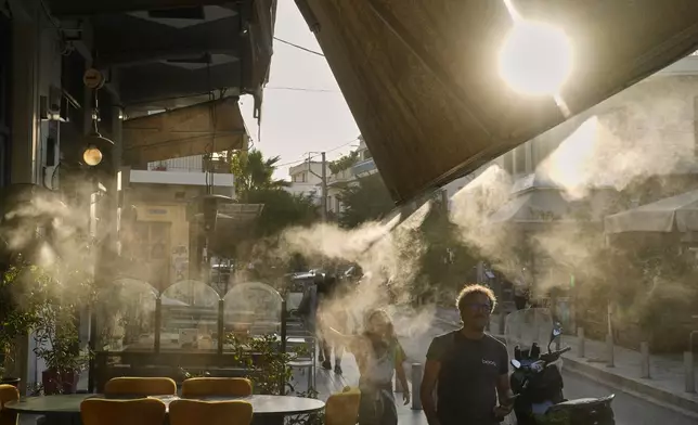 Pedestrians walk next to a mist machine in Thisio district of Athens during a heatwave, Tuesday, July 22, 2025.(AP Photo/Petros Giannakouris)