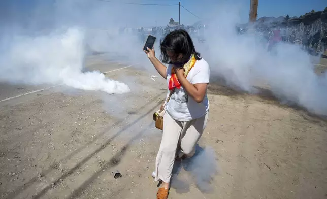 A protester runs from tear gas tossed by federal immigration agents to clear a path for the vehicles during a raid in the agriculture area of Camarillo, Calif., Thursday, July 10, 2025. (AP Photo/Michael Owen Baker)