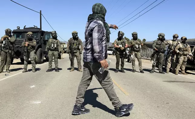 A demonstrator walks in front of federal agents blocking a road during an immigration raid in Camarillo, Calif., Thursday, July 10, 2025. (AP Photo/Michael Owen Baker)