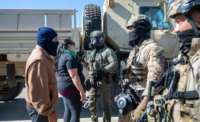 Federal immigration agents talk to Rebecca Torres, second left, after she tried to block a military vehicle during a raid in the agriculture area of Camarillo, Calif., Thursday, July 10, 2025. (AP Photo/Michael Owen Baker)