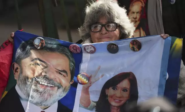 A supporter of Argentina's former President Cristina Fernandez holds a flag featuring Brazil's President Luiz Inacio Lula da Silva and Fernandez outside her home where she is under house arrest serving a six-year prison sentence for corruption, in Buenos Aires, Argentina, Thursday, July 3, 2025, on the day Lula visited her at home while he is in the country for the Mercosur Summit. (AP Photo/Rodrigo Abd)