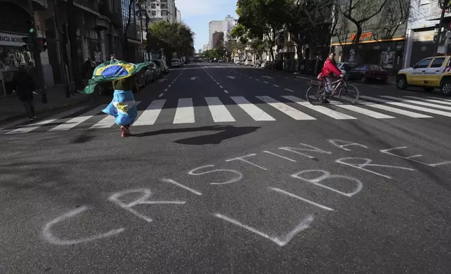 A woman holds up a Brazilian flag on a road covered by the Spanish phrase: "Free Cristina" near the home of former President Cristina Fernandez, who is under house arrest serving a six-year prison sentence for corruption, after Brazil's President Luiz Inacio Lula da Silva visited her in Buenos Aires, Argentina, Thursday, July 3, 2025. (AP Photo/Rodrigo Abd)