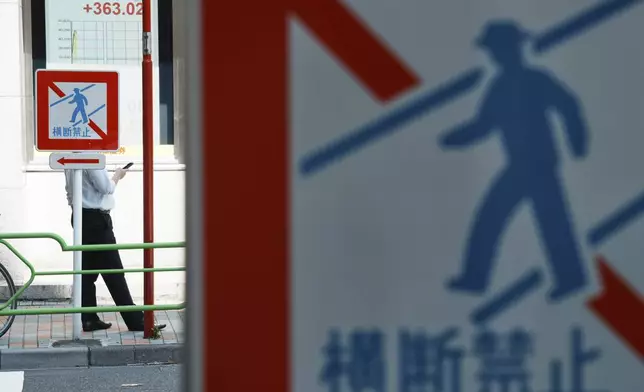 A person stands near an electronic stock board, left top, showing Japan's Nikkei index at a securities firm Tuesday, July 22, 2025, in Tokyo. The traffic signs read: No Crossing. (AP Photo/Eugene Hoshiko)