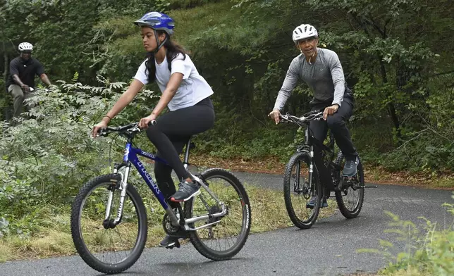 FILE - President Barack Obama follows his daughter Malia Obama as they rides bikes in West Tisbury, Mass., on Martha's Vineyard, Aug. 22, 2015, during the Obamas annual vacation. (AP Photo/Susan Walsh, File)