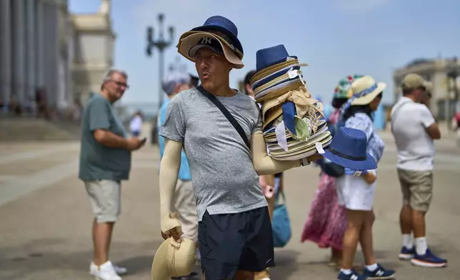A vendor sells hats during a heat wave in Madrid, Spain, Tuesday, July 1, 2025. (AP Photo/Manu Fernandez)