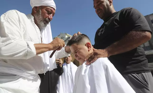 A Lebanese Shiite boy winces as a man prepares to cut his head with a razor during Ashoura, the Shiite Muslim commemoration marking the 7th-century death of Imam Hussein, the grandson of the Prophet Muhammad, at the Battle of Karbala, in the southern market town of Nabatiyeh, Lebanon, Sunday, July 6, 2025. (AP Photo/Mohammad Zaatari)
