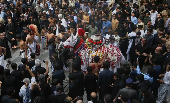 Shiite Muslims touch a horse, that symbolizes the horse that carried Imam Hussein during the battle of Karbala, at an Ashoura procession, in Peshawar, Pakistan, Sunday, July 6, 2025. (AP Photo/Muhammad Sajjad)