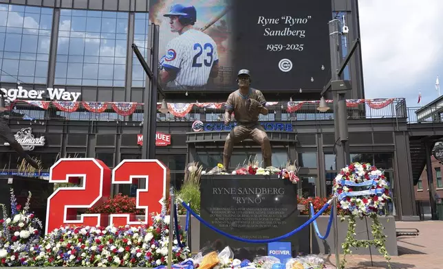 Fans leave flowers and other items at a makeshift memorial in front of the statue of Chicago Cubs' Hall of Fame second baseman Ryne Sandberg, Tuesday, July 29, 2025, outside Wrigley Field in Chicago. (AP Photo/Nam Y. Huh)