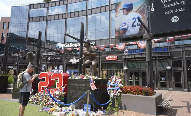 Fans visit as they leave flowers and other items at a makeshift memorial in front of the statue of Chicago Cubs' Hall of Fame second baseman Ryne Sandberg, Tuesday, July 29, 2025, outside Wrigley Field in Chicago. (AP Photo/Nam Y. Huh)