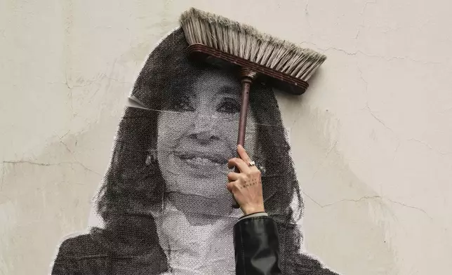 A supporter of Argentina's former President Cristina Fernandez uses a broom to paste a photo of her on the wall outside her home in Buenos Aires, Argentina, Tuesday, June 17, 2025. (AP Photo/Natacha Pisarenko)