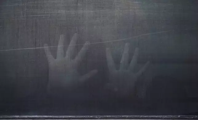A woman from Peru signals through the barred and tinted windows of a bus after she was detained following an appearance at immigration court, Monday, June 23, 2025, in San Antonio. (AP Photo/Eric Gay)