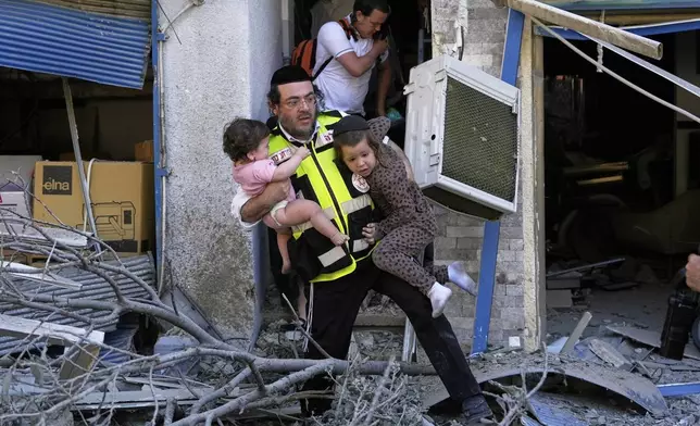 A rescue worker evacuates two children from the site where a missile launched from Iran struck in Haifa, Israel, Sunday, June 22, 2025. (AP Photo/Baz Ratner)