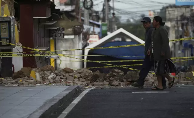 Neighbors walk past the rubble of a damaged house in Palin, Guatemala, Wednesday, July 9, 2025, after a series of earthquakes with magnitudes ranging from 3.0 to 5.6, according to authorities. (AP Photo/Moises Castillo)