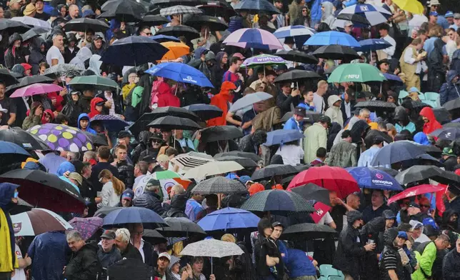 Fans stand with umbrella after heavy rain stopped play during the first day of the fifth cricket test match between England and India at The Kia Oval in London, Thursday, July 31, 2025. (AP Photo/Kirsty Wigglesworth)