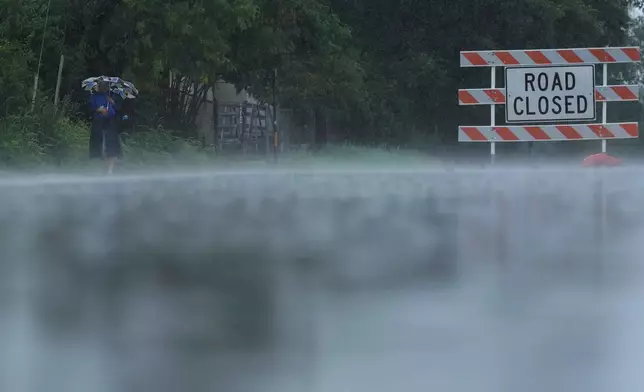 A woman walks in the rain past a closed street near the Guadalupe River, Sunday, July 13, 2025, in Kerrville, Texas. (AP Photo/Eric Gay)