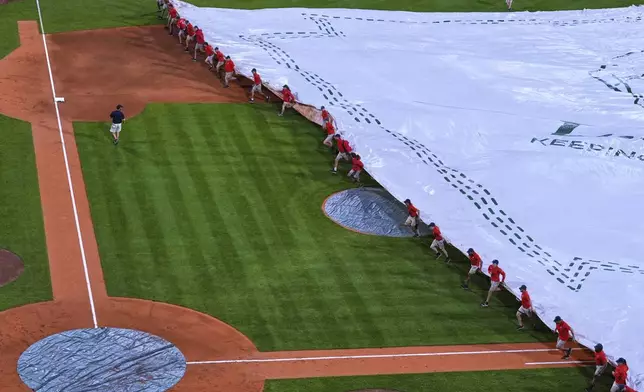 The grounds crew covers the field with a tarp during a rain delay in the fourth inning of a baseball game between the Boston Red Sox and Cincinnati Reds at Fenway Park, Tuesday, July 1, 2025, in Boston. (AP Photo/Charles Krupa)