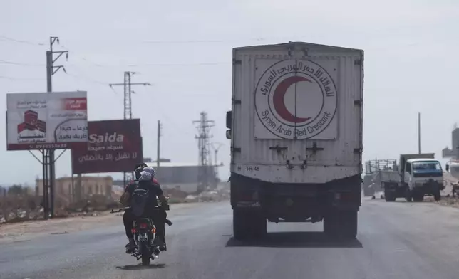 Fighters ride a motorcycle past a convoy of vehicles loaded with food and other aid en route to Sweida on the international highway in rural Daraa province, Syria, Sunday, July 20, 2025, heading to the city of Busra al-Sham. (AP Photo/Omar Sanadiki)