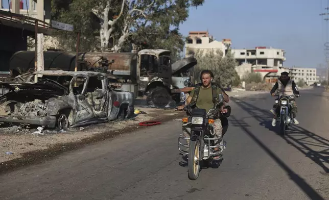 Bedouin fighters ride motorcycles past burned vehicles in Mazraa village on the outskirts of Sweida city, in southern Syria, Saturday, July 19, 2025. (AP Photo/Ghaith Alsayed)