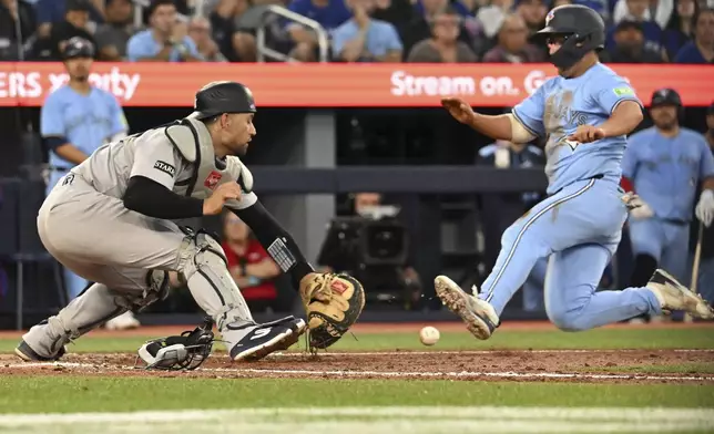 Toronto Blue Jays' Davis Schneider, right, scores a run ahead of a tag by New York Yankees catcher J.C. Escarra in the fifth inning of a baseball game in Toronto on Wednesday, July 23, 2025. (Jon Blacker/The Canadian Press via AP)
