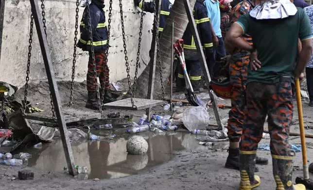 Firemen stand next to swing as they work at the site of a Bangladesh Air Force training aircraft that crashed into a school campus shortly after takeoff in Dhaka, Bangladesh, Monday, July 21, 2025. (AP Photo/Mahmud Hossain Opu)