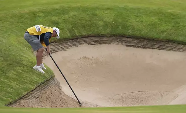Jason Reynolds caddie for Dean Burmester of South Africa rakes a bunker on the 1st after Burmester played a shot from it during the third round of the British Open golf championship at the Royal Portrush Golf Club, Northern Ireland, Saturday, July 19, 2025. (AP Photo/Jon Super)