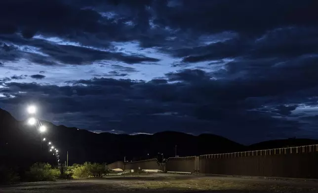 A section of the U.S.-Mexico border fence is illuminated by lights at dawn on Wednesday, July 23, 2025, in Sunland Park, N.M. (AP Photo/Jae C. Hong)