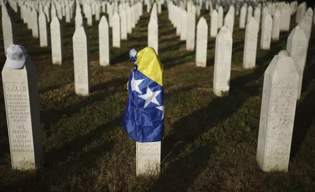 A Bosnian flag is seen at a grave stone at the Memorial Center for those killed in Srebrenica genocide in Potocari, Bosnia, Friday, July 11, 2025. (AP Photo/Armin Durgut)