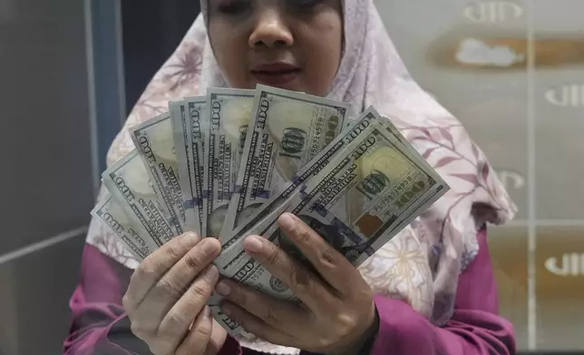 An employee shows US dollar bills at a money changer in Jakarta, Indonesia, Wednesday, July 16, 2025. (AP Photo/Tatan Syuflana)