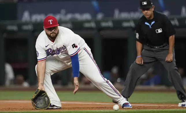 Texas Rangers first baseman Rowdy Tellez, left, fields a groundout by Detroit Tigers' Riley Greene as umpire Carlos Torres, right, looks on in the first inning of a baseball game, Saturday, July 19, 2025, in Arlington, Texas. (AP Photo/Tony Gutierrez)