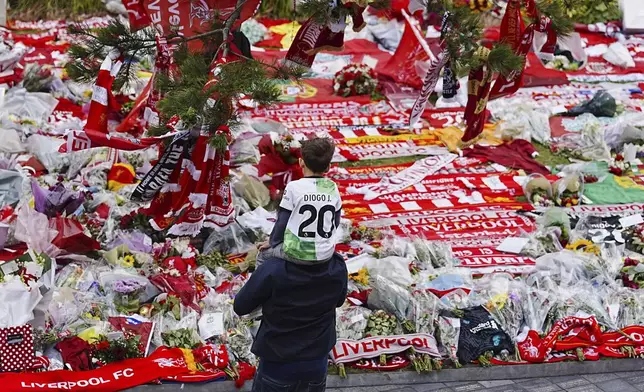 A boy wearing a jersey with the name of Liverpool and Portugal player Diogo Jota, sits on a man's shoulders as they look at tributes in memory of Jota, who died in a car crash with his brother in Spain in the early hours of Thursday, at Anfield Stadium, England, Sunday, July 6, 2025. (Peter Byrne/PA via AP)