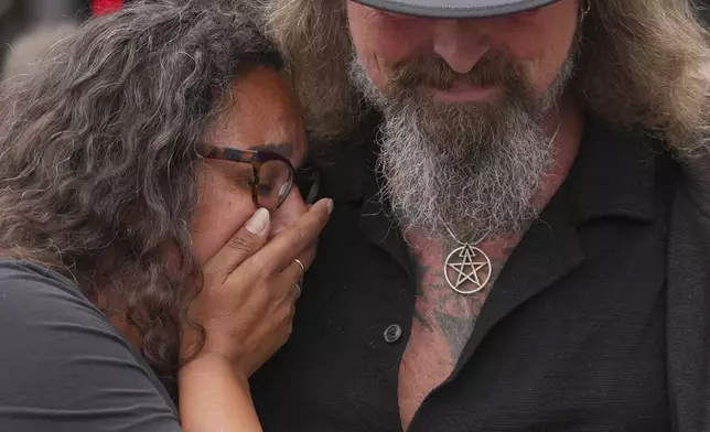 Music fans react after they lay flowers to commemorate the death of Ozzy Osbourne at the Black Sabbath Bridge in Birmingham, Wednesday, July 23, 2025. (AP Photo/Kin Cheung)