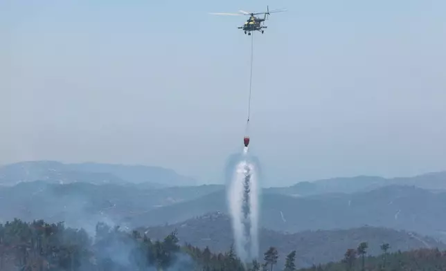 A Syrian helicopter drops water to extinguish a forest fire in the town of Rabia, in Syria's Latakia countryside, Saturday, July 12, 2025. (AP Photo/Ghaith Alsayed)