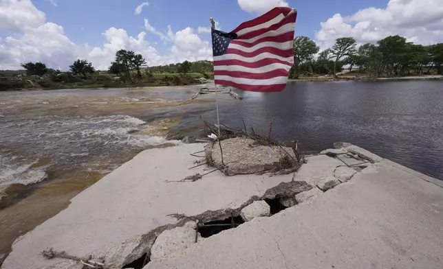 An American flag sits on a destroyed bridge over the Guadalupe River at Arcadia Loop and Bear Creek Road after flooding in Kerrville, Texas on Wednesday , July 9, 2025. (AP Photo/Gerald Herbert)