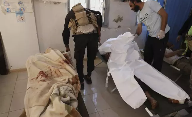 A Syrian government soldier, left, and a civilian man right, check dead bodies who were killed in Sweida city during clashes between the Syrian government forces and Druze militias, at a clinic in Busra al-Harir village, southern Syria, Tuesday, July 15, 2025. (AP Photo/Omar Albam)