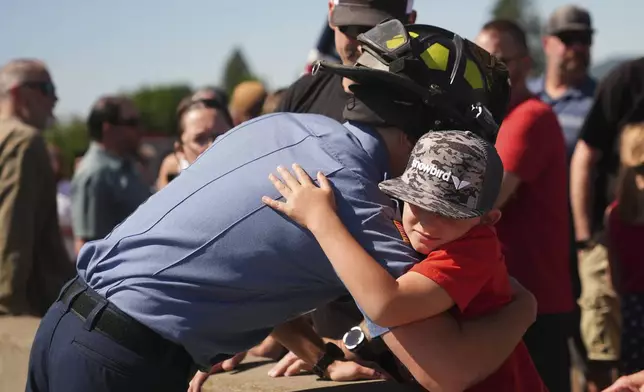 Coeur d'Alene firefighter Cody Moore greets friends, Troy Serticchio and Brayden, 8, as a crowd gathers to honor the firefighters who were killed Sunday, in Coeur d'Alene, Idaho, on Tuesday, July 1, 2025. (AP Photo/Lindsey Wasson)