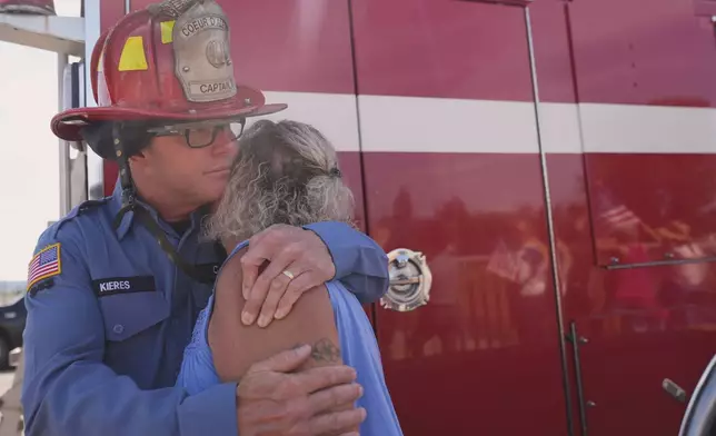 Kerry Kieres hugs her husband, Chris Kieres captain with Couer d'Alene Fire Dept., as a crowd gathers to honor the firefighters who were killed Sunday, in Coeur d'Alene, Idaho, on Tuesday, July 1, 2025. (AP Photo/Lindsey Wasson)