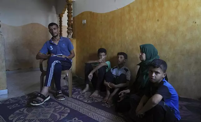 Hatem Al-Nouri, the father of two children who were killed, and one injured, in an Israeli strike while waiting to receive nutritional supplements at a medical clinic, sits with his family during an interview at his home in Deir al-Balah, Gaza Strip, Friday, July 11, 2025. (AP Photo/Abdel Kareem Hana)