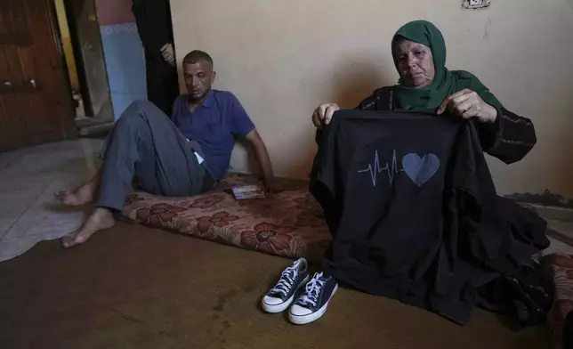 Nahla Al-Nouri shows the clothes of 13-year-old Sama, one of her three grandchildren who were killed in an Israeli strike while waiting to receive nutritional supplements at a medical clinic, during an interview at the family home in Deir al-Balah, Gaza Strip, Friday, July 11, 2025. (AP Photo/Abdel Kareem Hana)