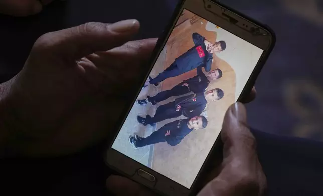 Hatem Al-Nouri shows a photo of his children Amir, 4, right, and Omar, 8, second from right, accompanied by their brothers, as he talks about when Hatem and Amir were killed in an Israeli strike while waiting to receive nutritional supplements at a medical clinic, during an interview at his home in Deir al-Balah, Gaza Strip, Friday, July 11, 2025. (AP Photo/Abdel Kareem Hana)