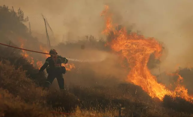 A firefighter uses a hose as he tries to extinguish the blaze near the town of Ierapetra on the south coast of Crete island, Greece, Thursday July 3, 2025, as a fast-moving wildfire prompted authorities to clear villages and coastal areas, officials said. (InTime News via AP)