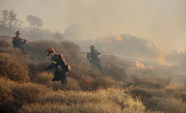 Firefighter uses a hose as the try to extinguish the blaze near the town of Ierapetra on the south coast of Crete island, Greece, Thursday July 3, 2025, as a fast-moving wildfire prompted authorities to clear villages and coastal areas, officials said. (InTime News via AP)
