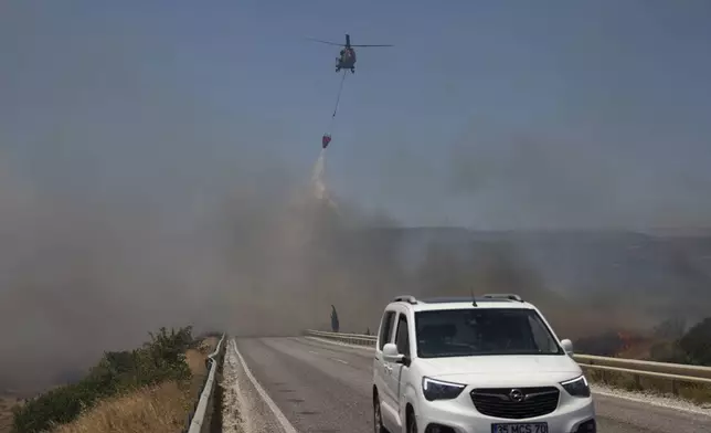 A helicopter drops water to extinguish a fire in Cesme, near Izmir, Turkey, Thursday, July 3, 2025. (Cengiz Malgir/Dia Photo via AP)