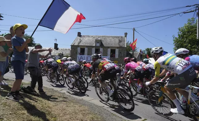 A boy waves a French flag as the pack rides during the sixth stage of the Tour de France cycling race over 201.5 kilometers (125.2 miles) with start in Bayeux and finish in Vire Normandy, France, Thursday, July 10, 2025. (AP Photo/Thibault Camus)